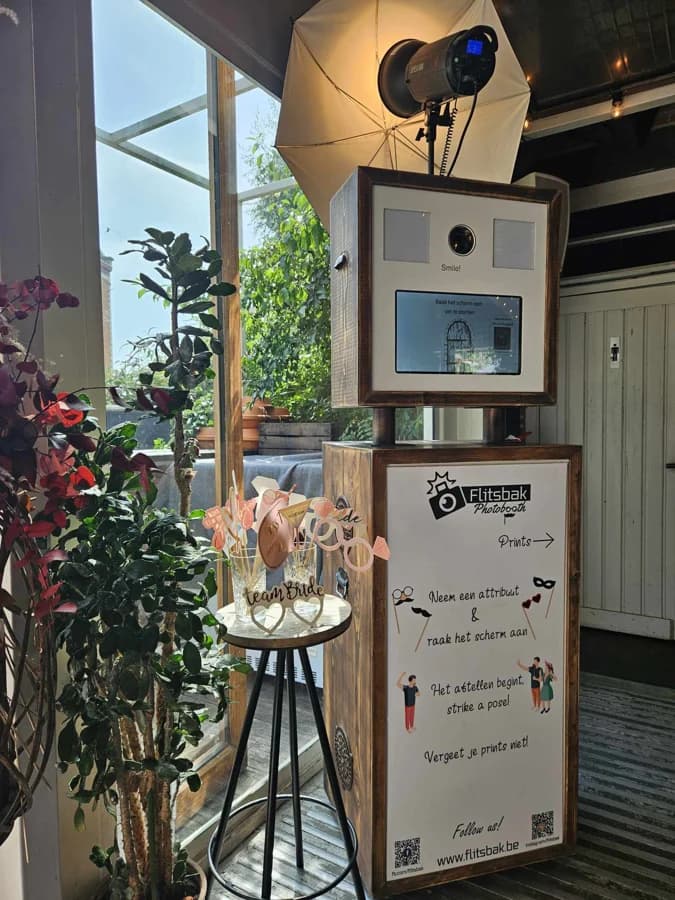 Flitsbak V1 op locatie: houten kast met camera, scherm, flits met paraplu, een bord met instructies en een tafeltje met props
