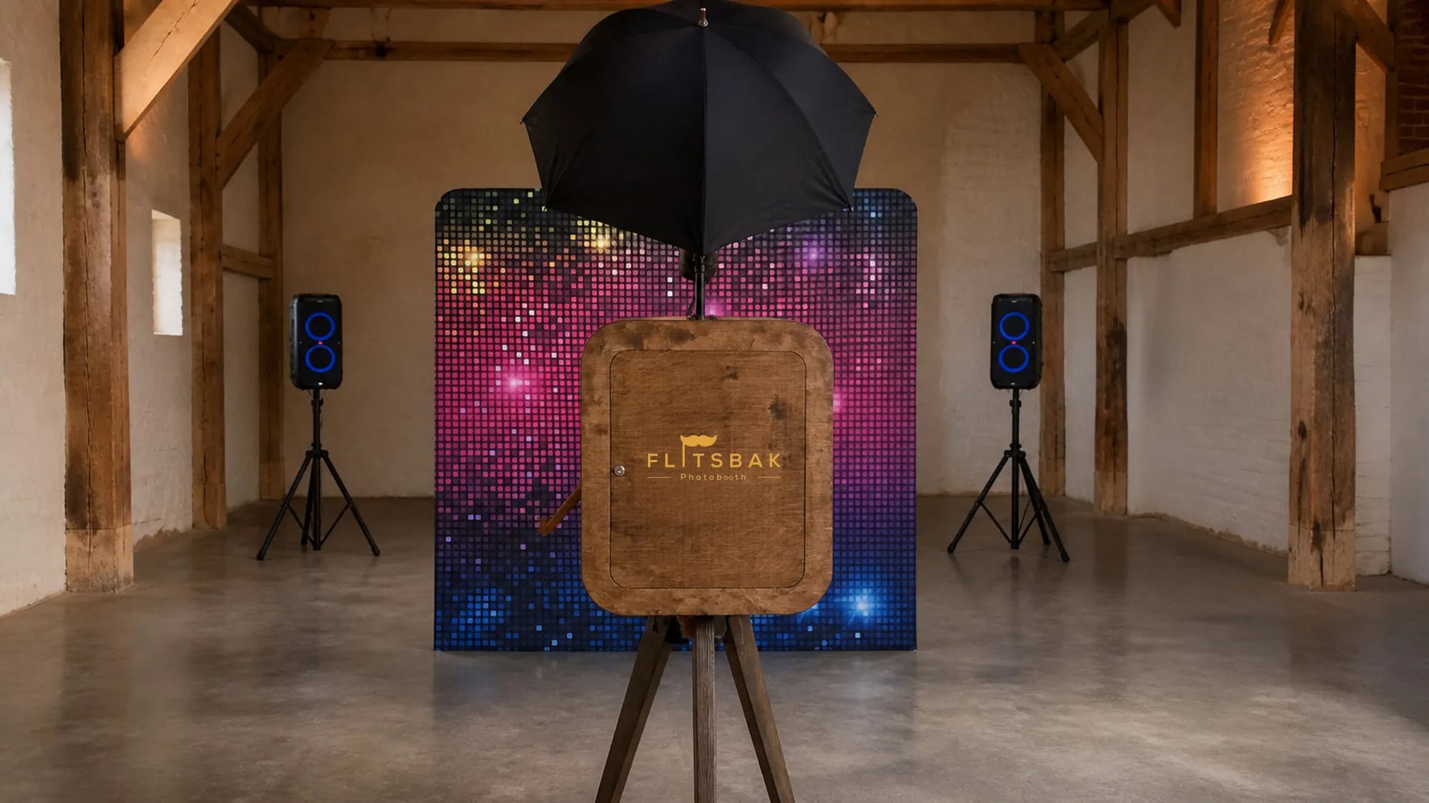 De Flitsbak photobooth met glitterwand-achtergrond en twee JBL PartyBox-speakers in een balkenzaal